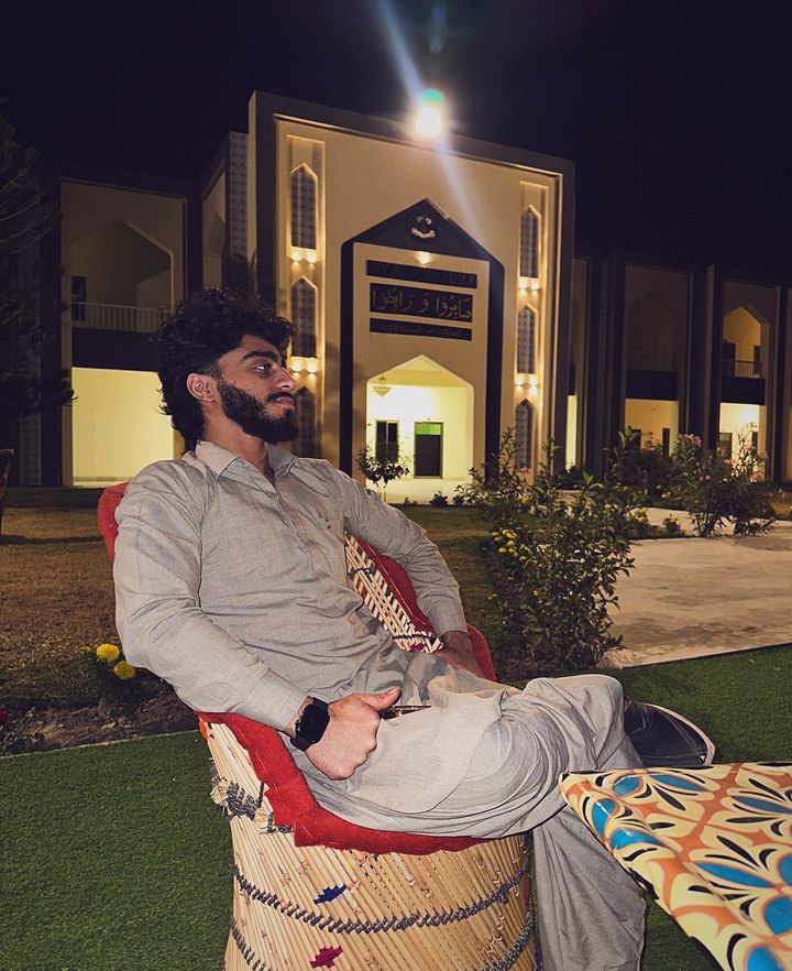 YNGMOMO (YNGM0M0) relaxing in a grey shalwar kameez outside a lit building in Pakistan at night